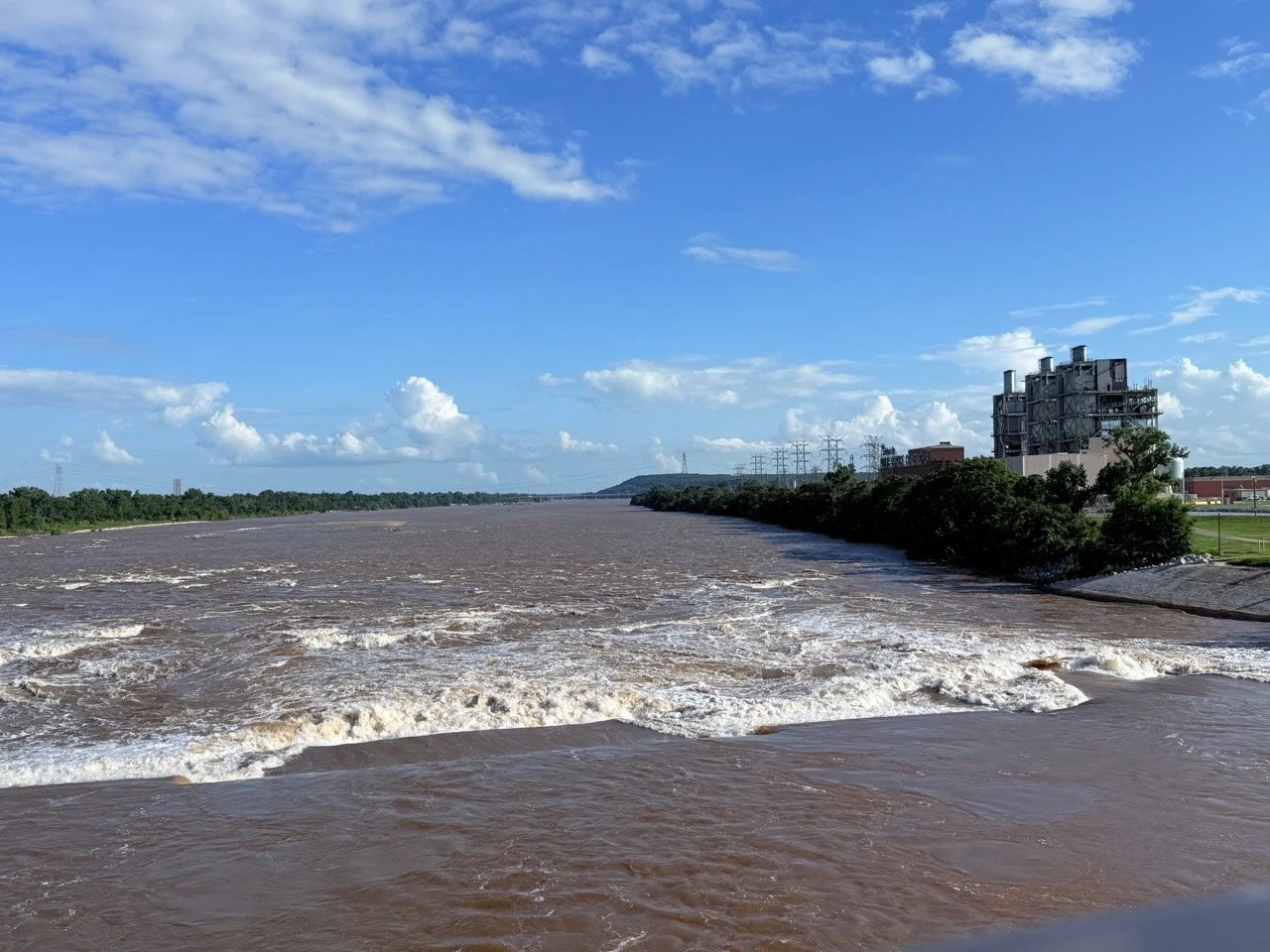 River rapids with trees and an industrial facility along the bank