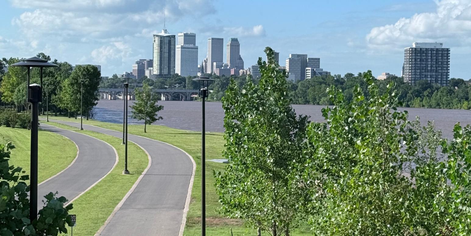 Tulsa skyline across the Arkansas River, with green grass and a riverside walking path